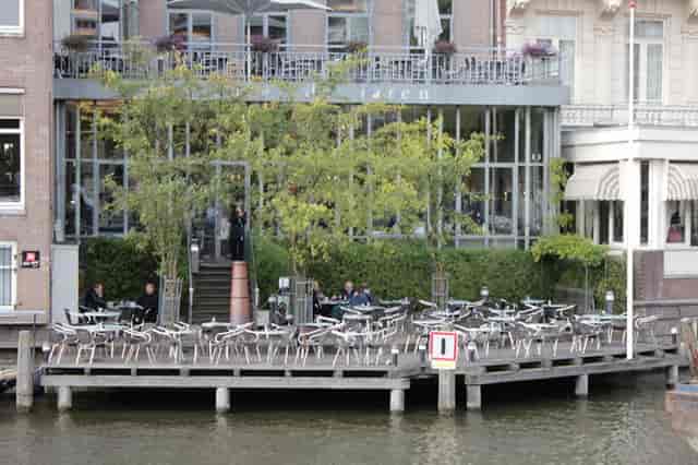 Stylish café balcony with outdoor terrace by waterway, perfect for networking events.
