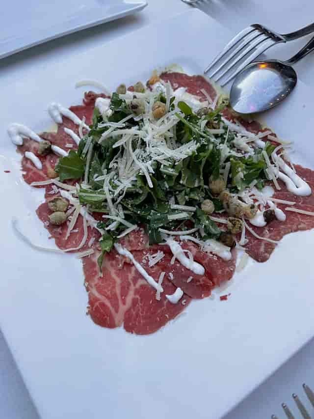 Beef carpaccio garnished with arugula and cheese, perfect for corporate dinners.