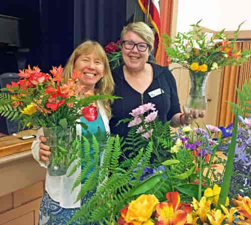 Smiling women with floral arrangements at Redwood City Woman's Club event.