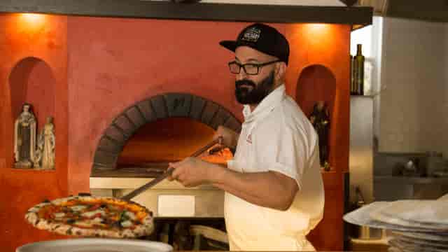 Pizzaiolo pulling pizza from a wood-fired oven at Diavola Dining Room event.