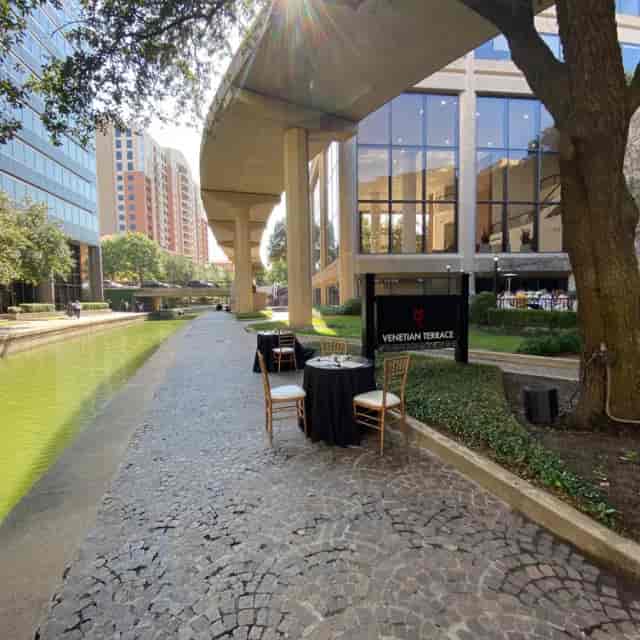 Outdoor patio at Venetian Terrace with tables by a serene waterway, perfect for events.