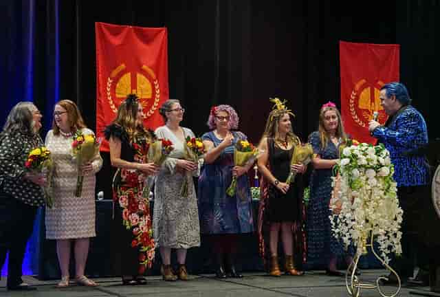 Diverse women on Flower Mound High School Theatre stage celebrate with bouquets and flags.