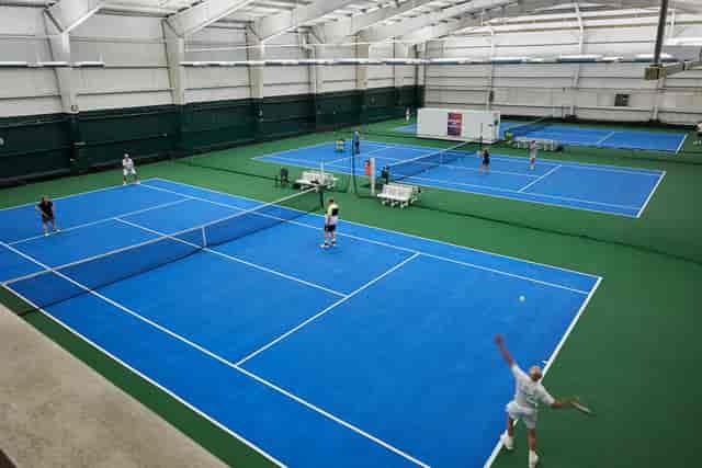 Indoor tennis facility with blue courts at Houston Racquet Club for sports events and tournaments.