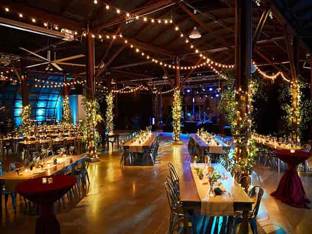 Rustic wedding venue with string lights, communal tables, stage.