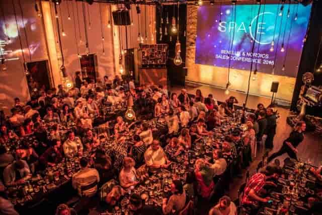 Corporate dinner setup at TOBACCO Theater with dramatic overhead lighting and projection screen.