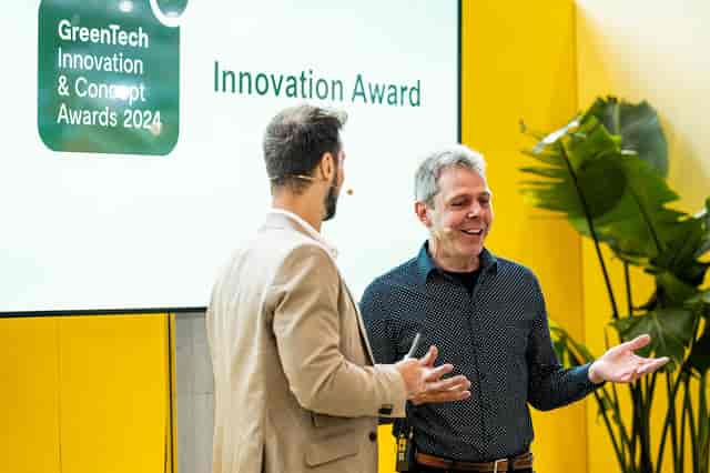Moderator hosting Australia-Netherlands GreenTech award ceremony on branded green event stage.