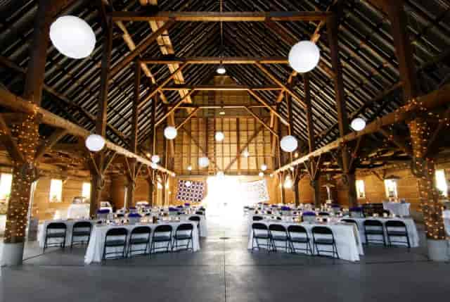 Rustic barn VIP event venue with banquet seating and warm string lighting.