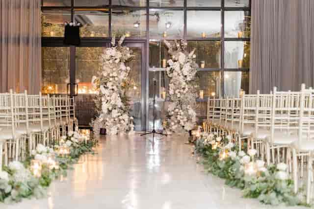 Grand Estate Ballroom wedding ceremony with floral pillars and white Chiavari chairs.