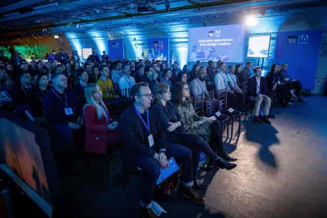 Engaged audience at a conference in The Postal Museum with blue lighting and stage setup.
