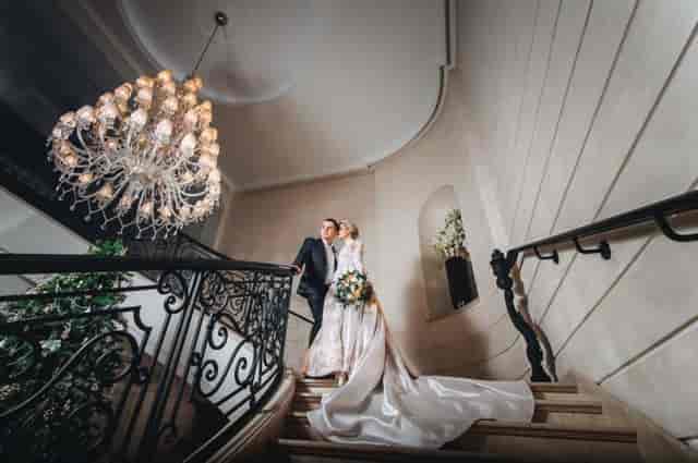 Luxury bridal staircase with ornate ironwork and chandelier for high-end wedding event venue.