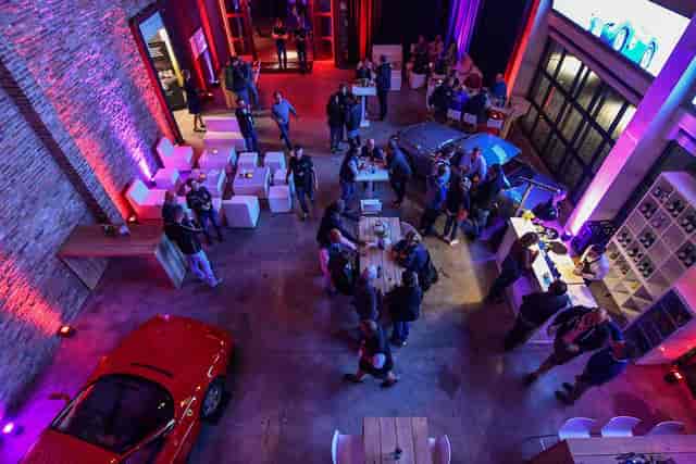Industrial automotive venue for evening networking event with creative LED lighting and car display.