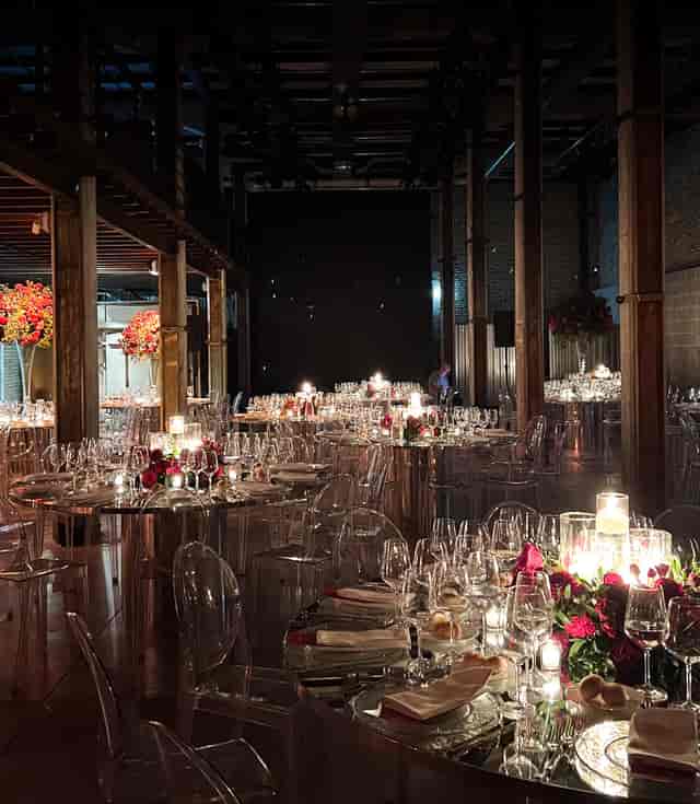 Industrial-chic banquet hall with ghost chairs and mirrored tables for gala or wedding events.
