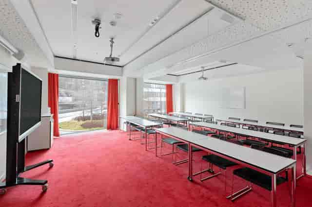 Classroom-style meeting room with red carpet, ideal for corporate workshops and training sessions.