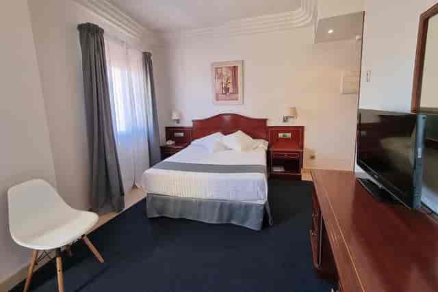 Hotel Gran Legazpi conference room with dark carpet and white bedding for budget event bookings.