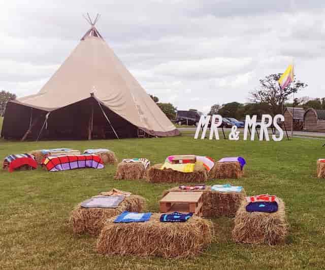 Rustic tipi wedding venue with hay bale seating for festival-style outdoor ceremonies.