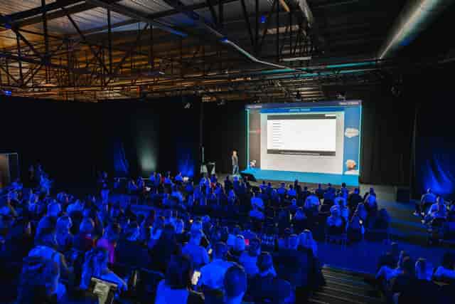 Corporate keynote presentation in a warehouse venue with mood lighting and large screen.