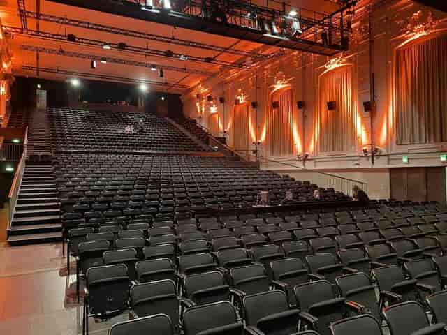 Tiered auditorium in Halle E with vibrant uplighting for corporate keynote or town hall events.