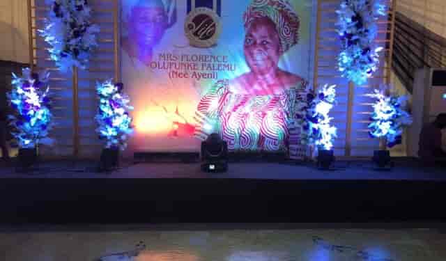 Memorial service stage with wood-slat backdrop and floral lighting for funeral event planning.