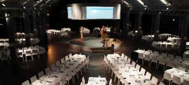 Industrial corporate banquet hall with central stage for gala dinners and event presentations.
