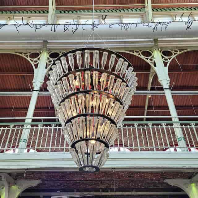 Upcycled glass-bottle chandelier at an industrial-chic event venue and exhibition space.