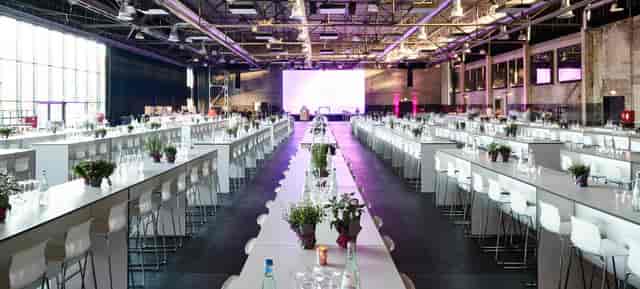 Industrial event venue in Motorworld Köln with communal tables and purple mood lighting.