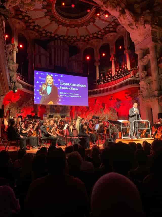 Awards ceremony with red lighting and orchestra in a historic Ronda Barcelona concert hall.