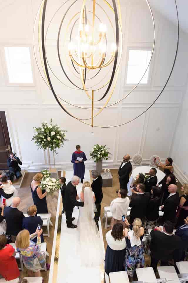 Wedding ceremony under statement chandelier at The Arlington Estate Heritage House ballroom.