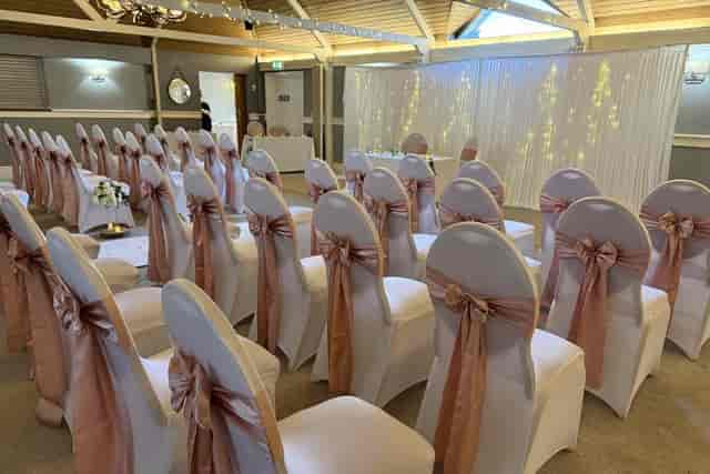 Main Hall wedding ceremony with rose-gold chair covers and illuminated backdrop.
