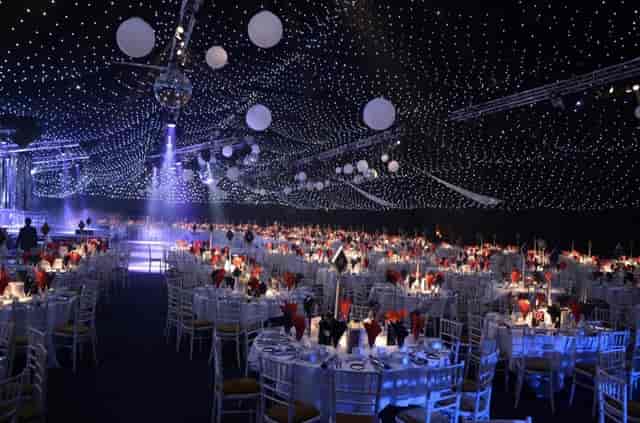 Elegant gala at Aintree Equestrian Centre with red floral centerpieces under starry canopy.