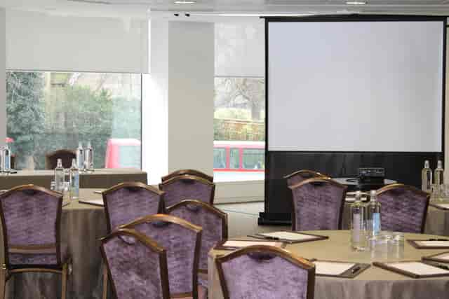 Beech Suite meeting space in Royal Lancaster London with round tables and large screen.
